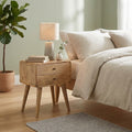 Curved oak-finish bedside table with 2 drawers next to a bed with linen bedding