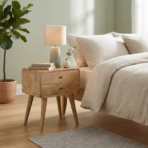 Curved oak-finish bedside table with 2 drawers next to a bed with linen bedding